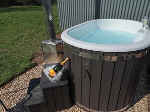 A hot tub with a champagne bottle and ice cubes in a glass container, surrounded by a wooden deck and a metal fence. - Dandelion (Grimsby)