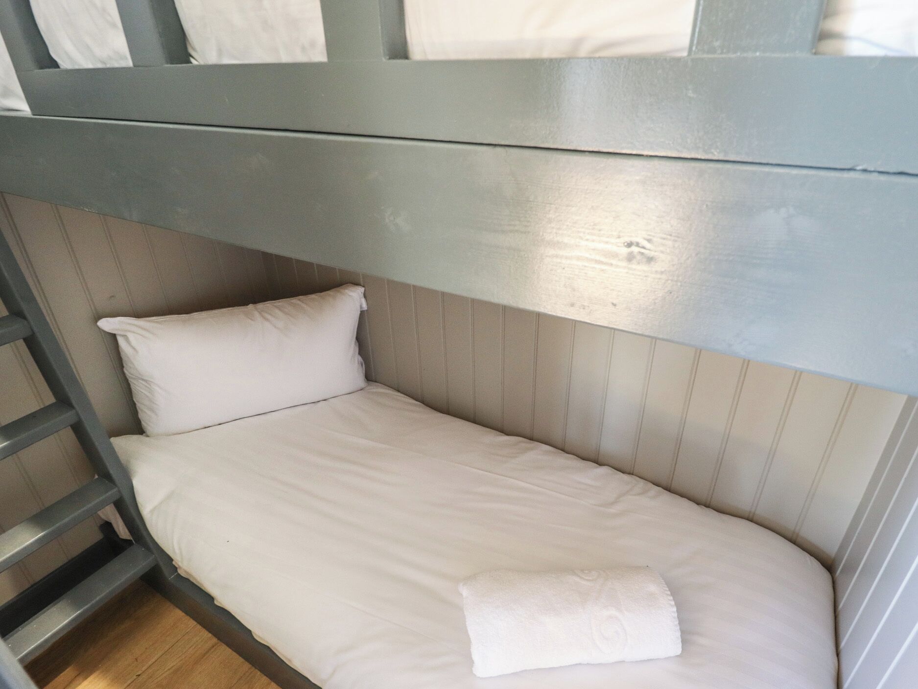 A bunk bed with a ladder, a single white pillow, and a neatly folded white towel.