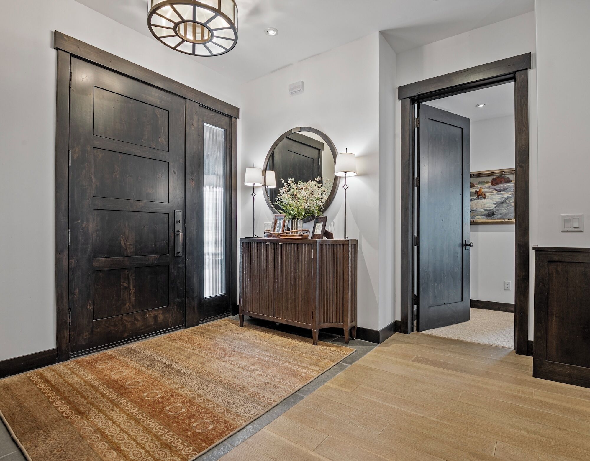 Un couloir avec des portes en bois fonc é, une console en bois surmontée d’un miroir et un tapis à motifs.