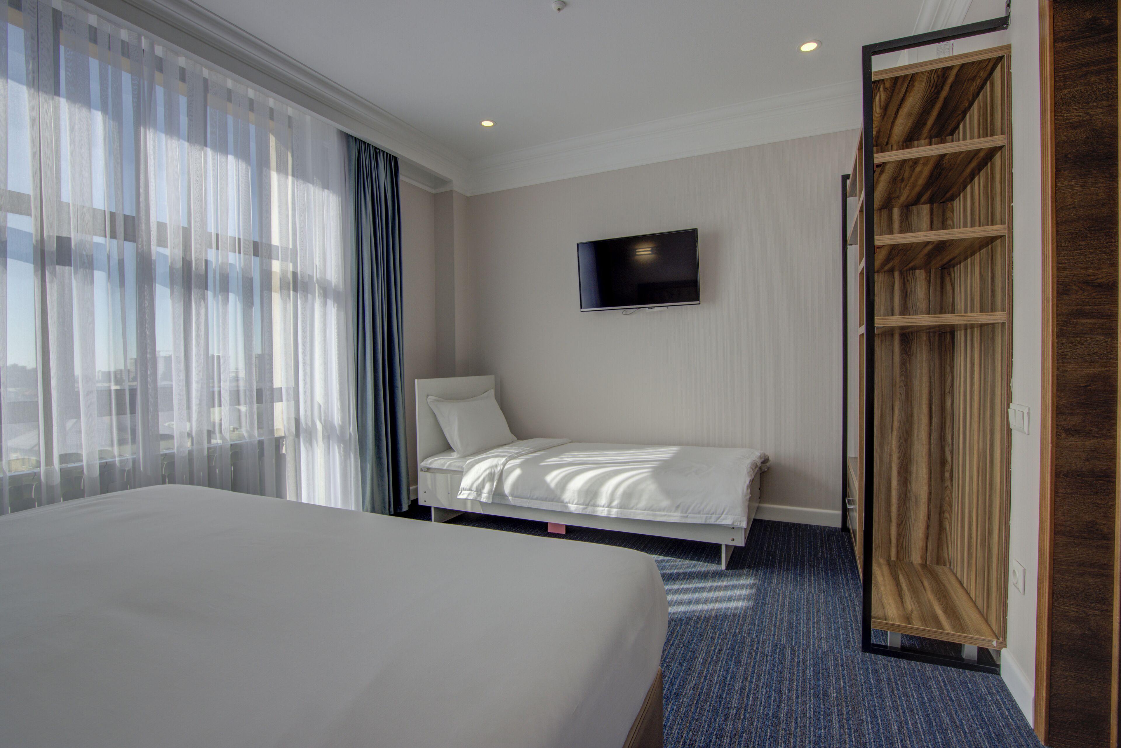 A hotel room with a large bed, a TV mounted on the wall, and a wooden wardrobe.