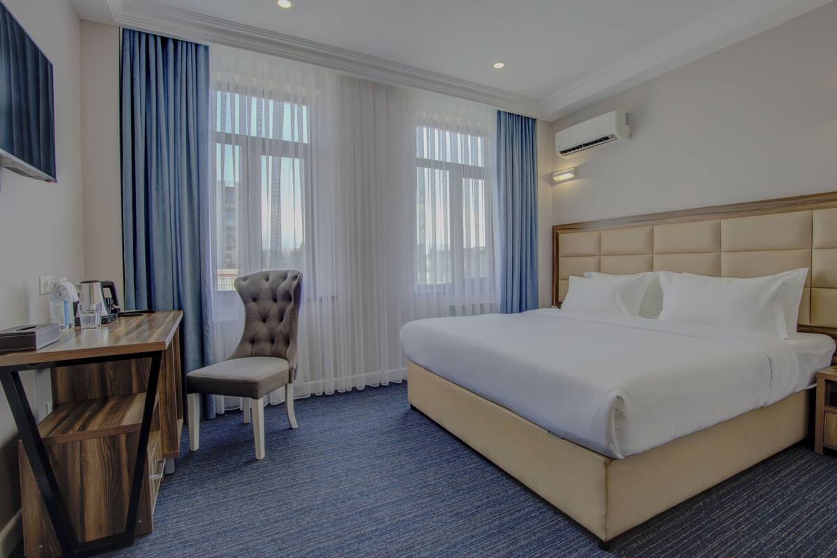 A hotel room with a large bed, a desk with a chair, and a window with curtains.