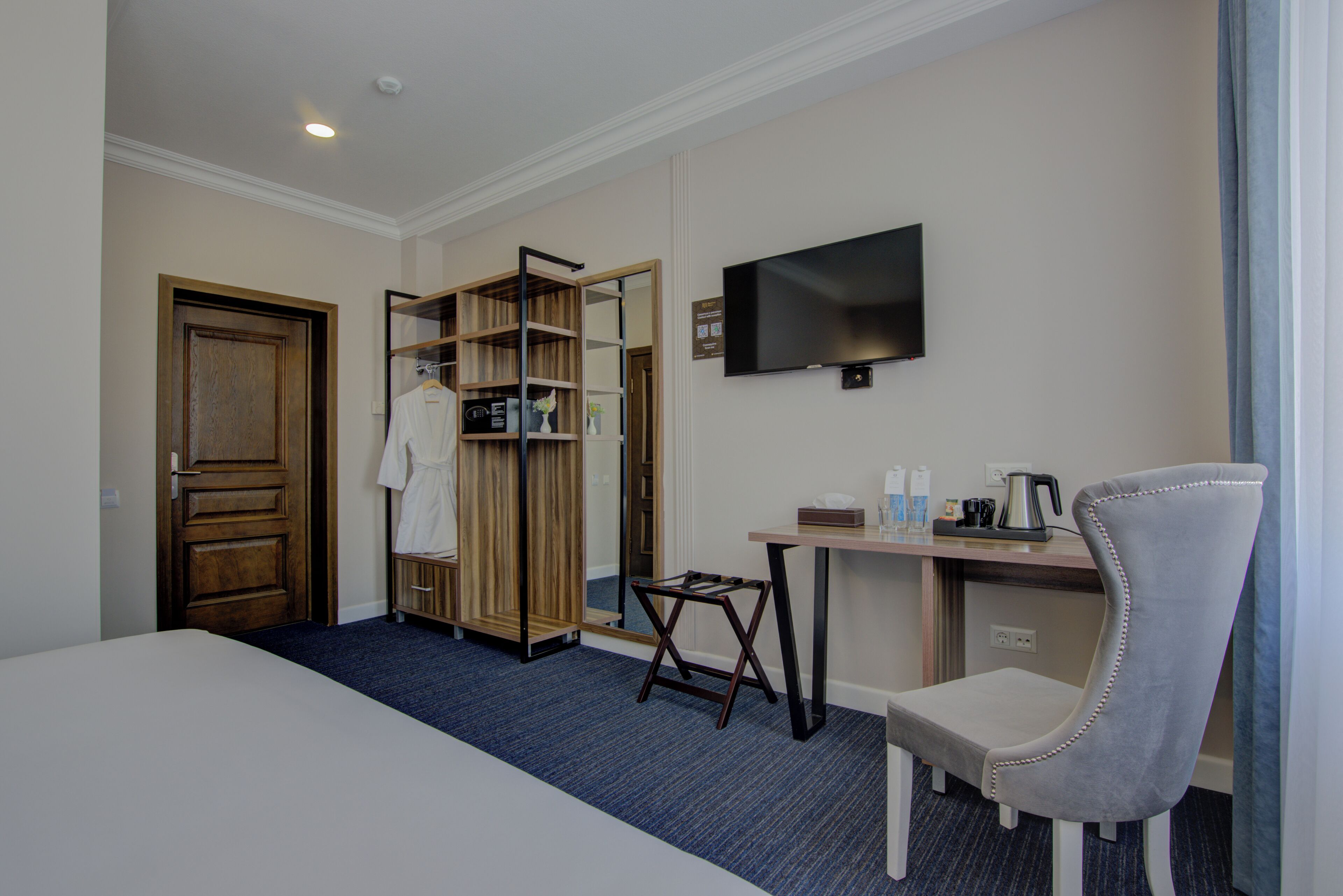 A hotel room with a bed, a desk, a chair, a TV, a wardrobe, and a mirror.