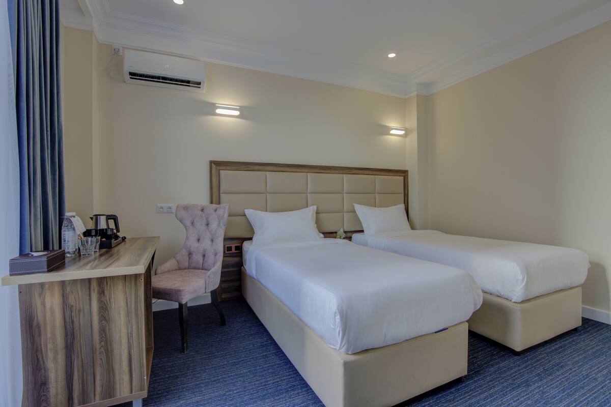 A hotel room with two beds, a desk, a chair, and an air conditioning unit.