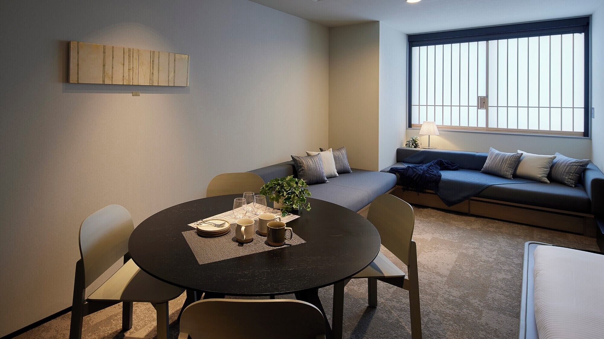 A modern living room with a round dining table, a sofa, and a window with vertical blinds.