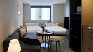 A compact hotel room with a sofa, two beds, a TV, and a small table with a lamp. - Minn Nihonbashi Suitengumae (Tokyo)
