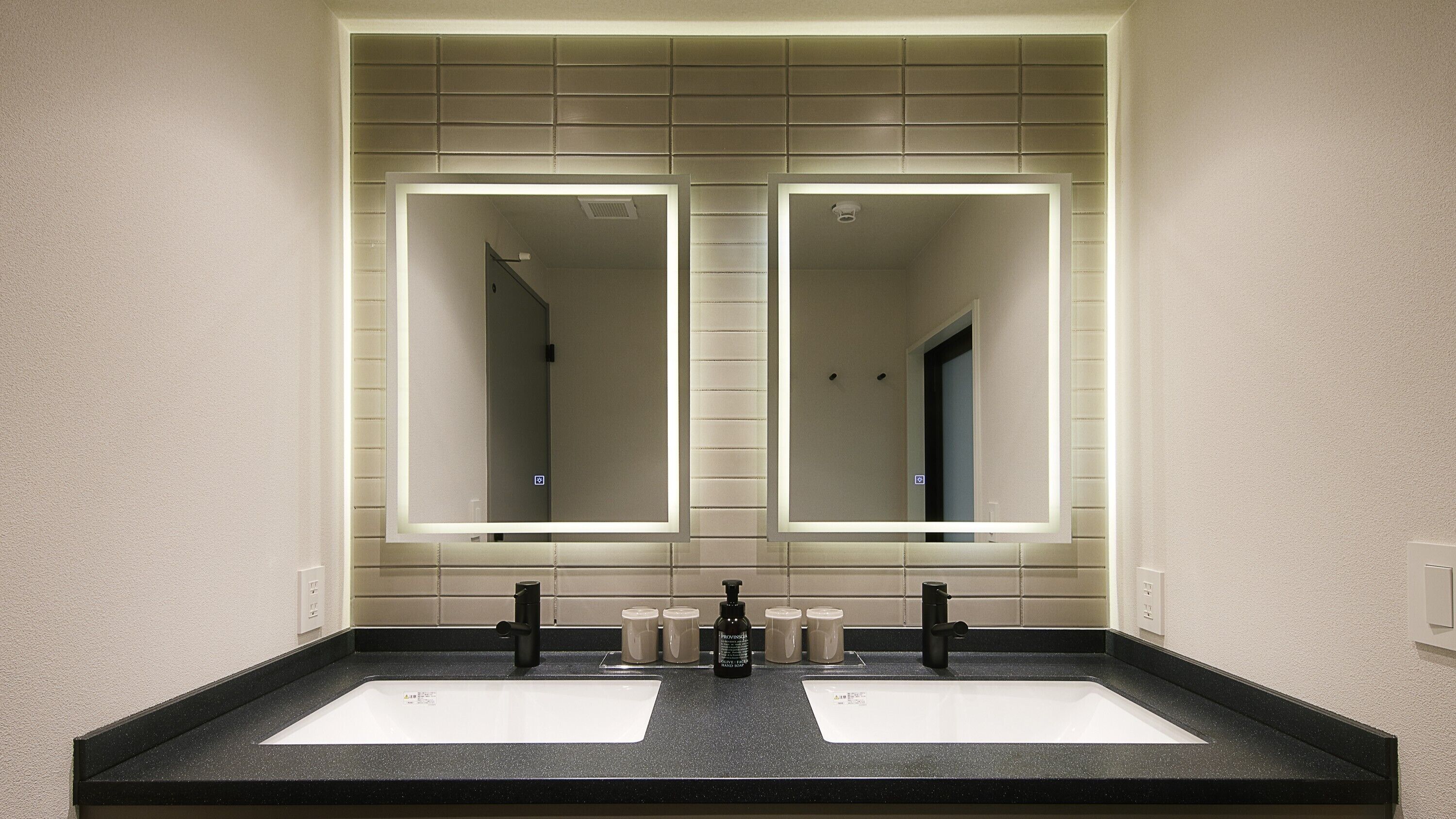 A bathroom with two sinks, a large mirror, and a black countertop.