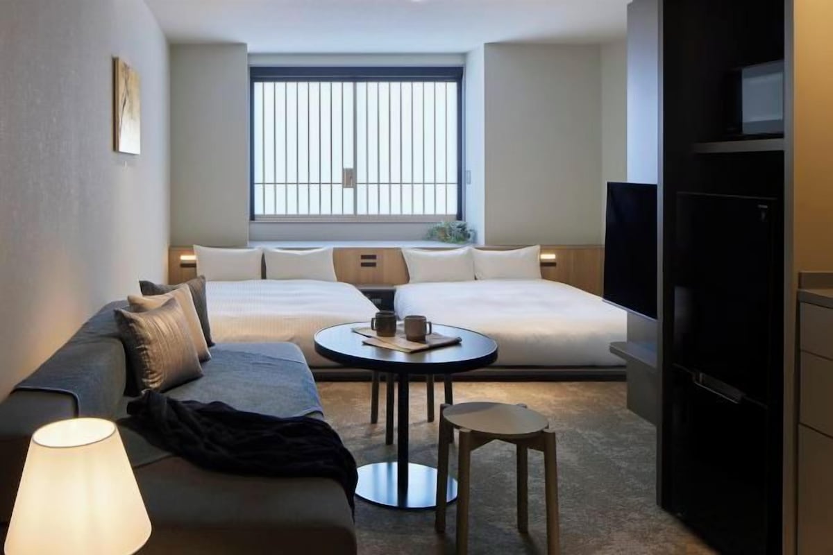 Een hotelkamer met twee bedden, een bank, een kleine tafel met een lamp en een televisie.