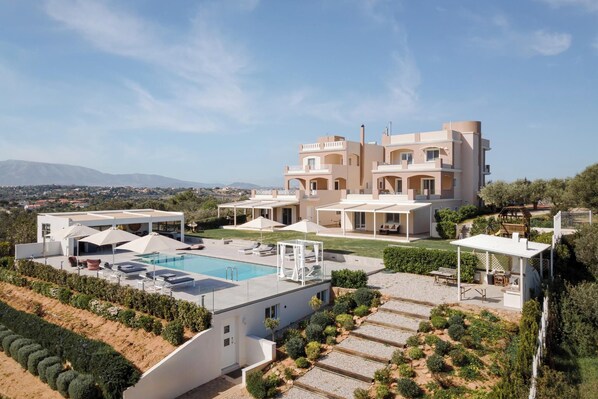 A modern villa with a swimming pool, outdoor seating, and a view of the surrounding landscape. - Ema's Guest House (Markopoulo Mesogaias)