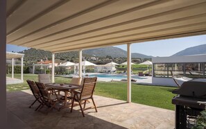 An outdoor patio with a pool, lounge chairs, and a grill area, overlooking a mountainous landscape. - Ema's Guest House (Markopoulo Mesogaias)