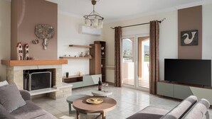 A living room with a fireplace, a television, and a balcony with curtains. - Ema's Guest House (Markopoulo Mesogaias)