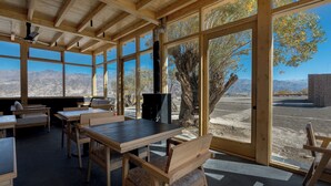 Un espace de restauration en plein air avec des tables et des chaises en bois, de grandes fenêtres et une vue sur les montagnes.