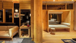 Un intérieur chaleureux en bois, avec un canapé, une petite table et une bouilloire, ainsi qu’un lit avec des oreillers.
