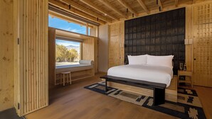 Une chambre à coucher moderne avec un grand lit, des poutres en bois au plafond, une vue sur les montagnes et une fenêtre donnant sur les arbres.