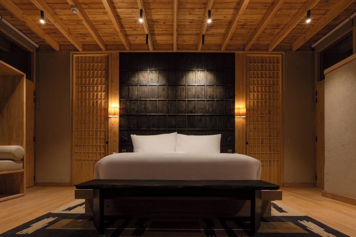 A hotel room with a large bed, wooden ceiling, and two wall-mounted lights.