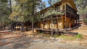 A two-story log cabin with a balcony, surrounded by trees and a gravel path.
