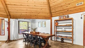 A dining area with a wooden table and chairs, a bookshelf, and a window with curtains.