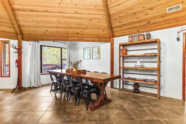 A dining area with a wooden table and chairs, a bookshelf, and a window with curtains.