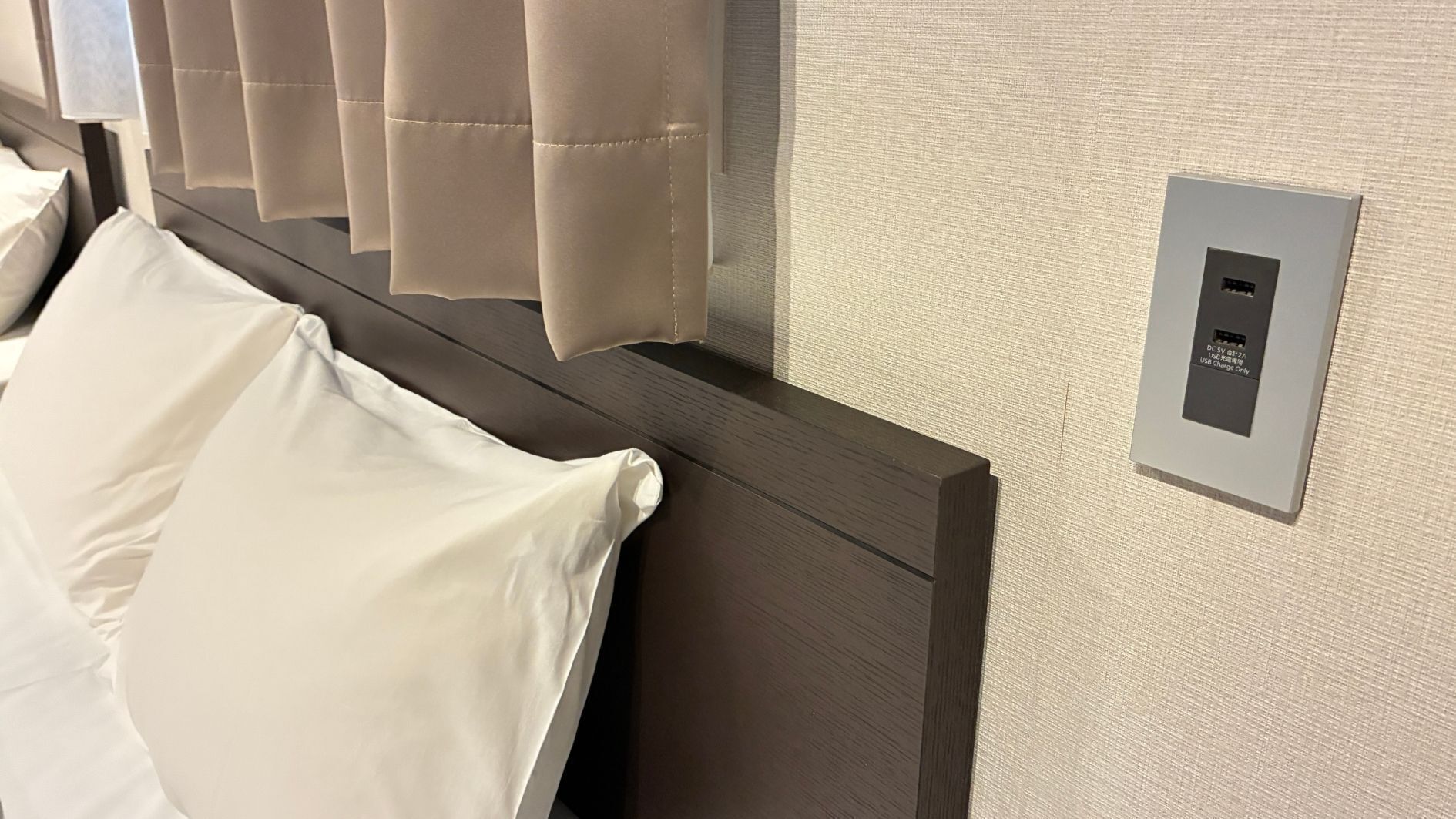A hotel room with a bed, a headboard, and a wall-mounted USB charging station.