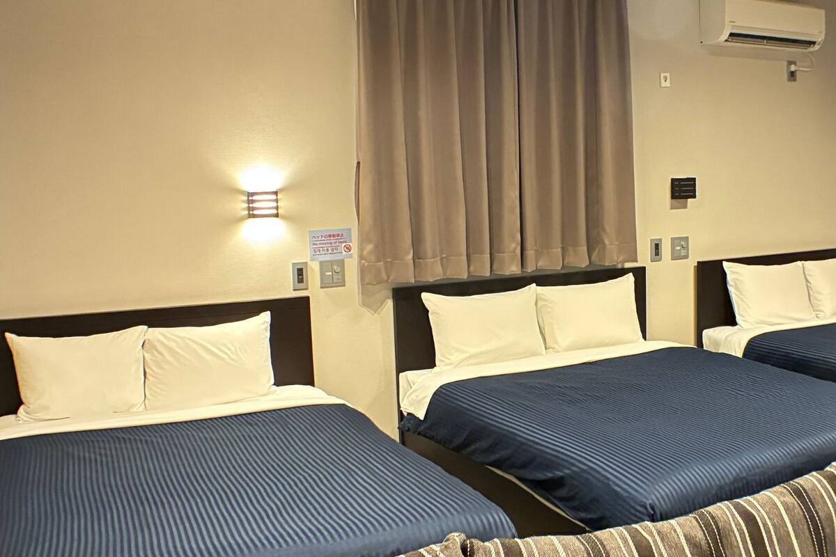 Habitación de hotel con dos camas, cada una con cabecera y almohadas, un aire acondicionado montado en la pared y una lámpara.