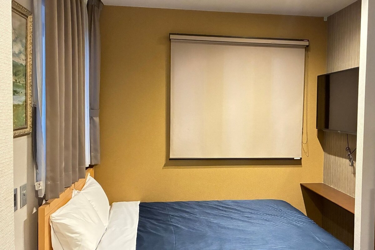 Ein Hotelzimmer mit einem Bett, einem Fernseher, einem Fenster mit Vorhängen und einem Bild an der Wand.