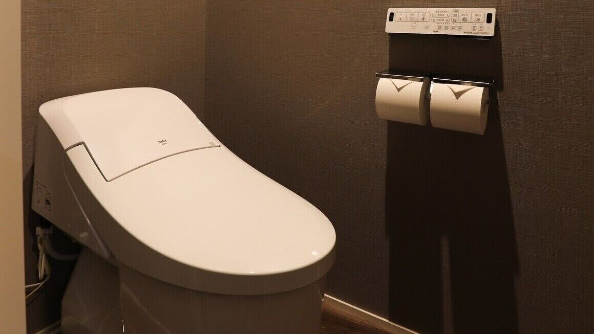 A modern toilet with a wall-mounted paper dispenser.