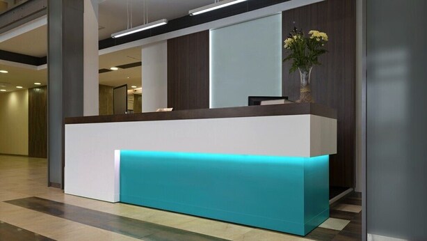 Een receptiebalie met een blauwgroene accentkleur, een vaas met gele bloemen en een modern interieur.