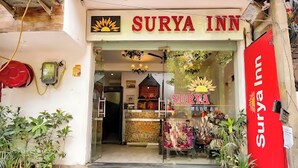 Het uiterlijk van Surya Inn, met een duidelijke ingang, een naamplaatje met de naam van het hotel en potplanten buiten.