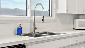 A kitchen with a stainless steel sink, a window, white cabinets, and a microwave.