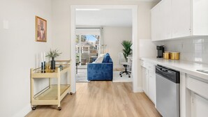 A modern kitchen with white cabinets, a dishwasher, and a coffee maker. There is a blue sofa in the adjacent living area.
