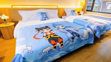 A hotel room with two beds, each with a blue bedspread featuring cartoon characters. There is a small wooden nightstand with a vase of flowers and a lamp.