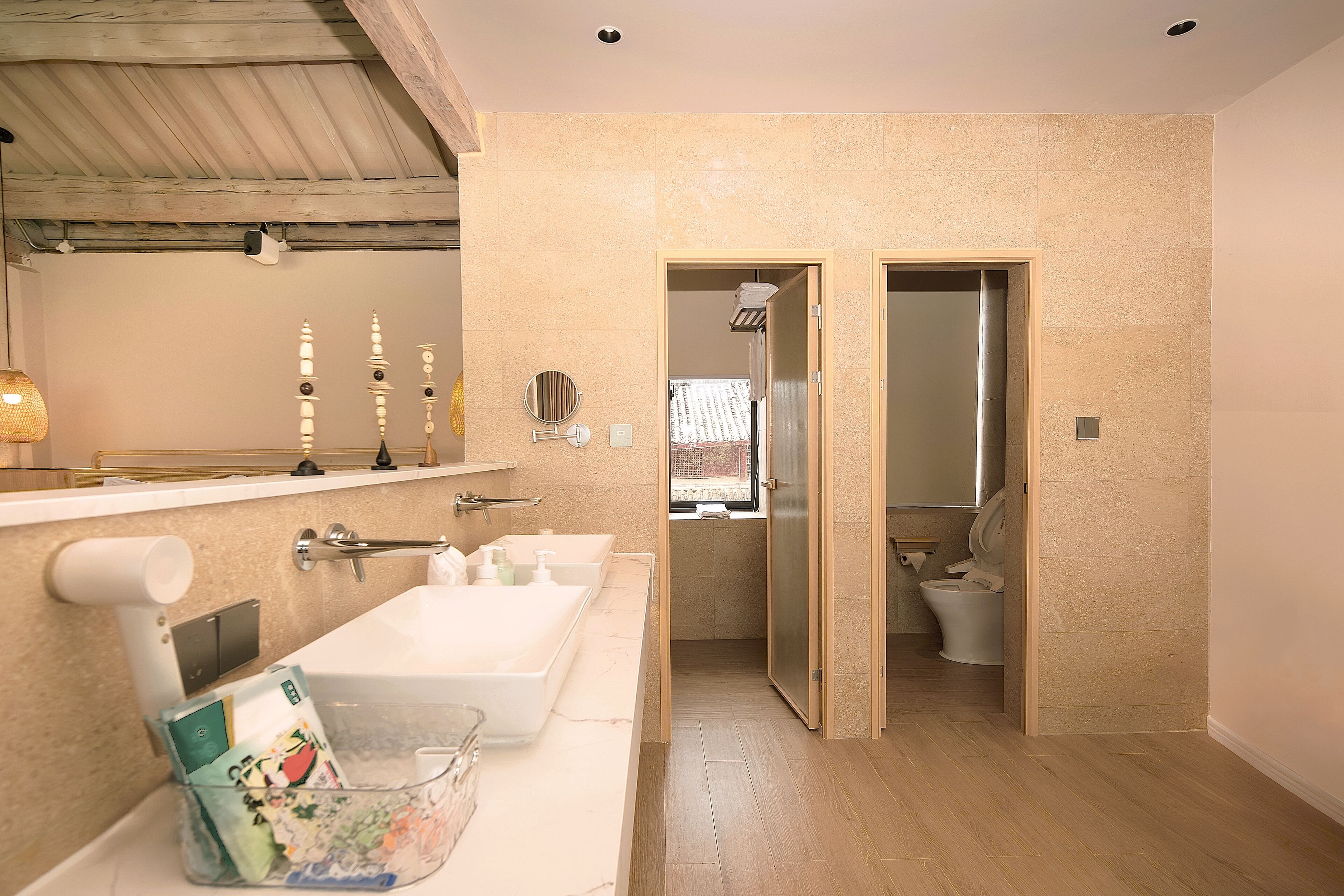 Un baño moderno con un espejo grande, dos lavamanos y un inodoro visible a través de una puerta abierta.