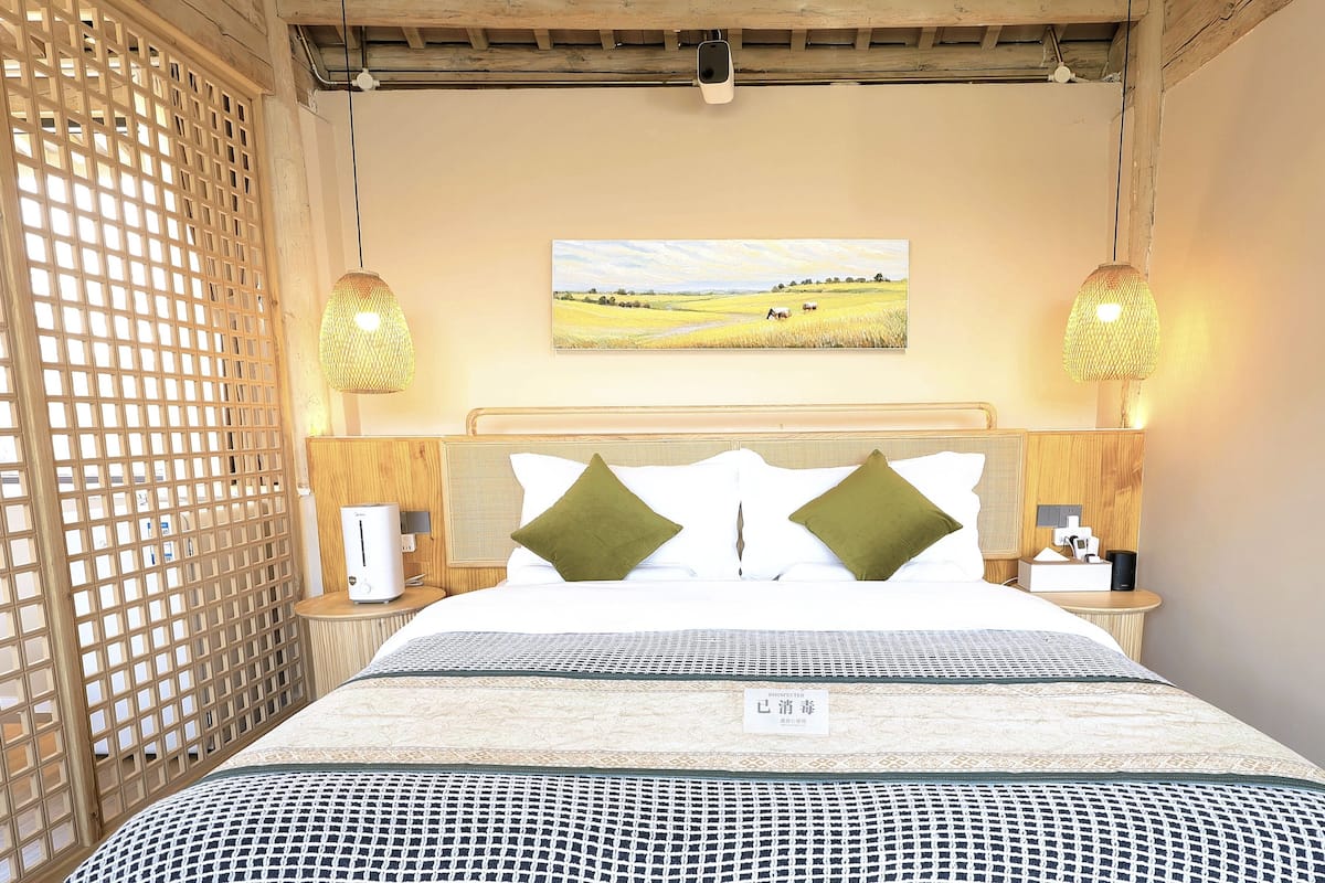Ein Hotelzimmer mit einem Bett, einem Gemälde von einem Feld und zwei Nachttischlampen.