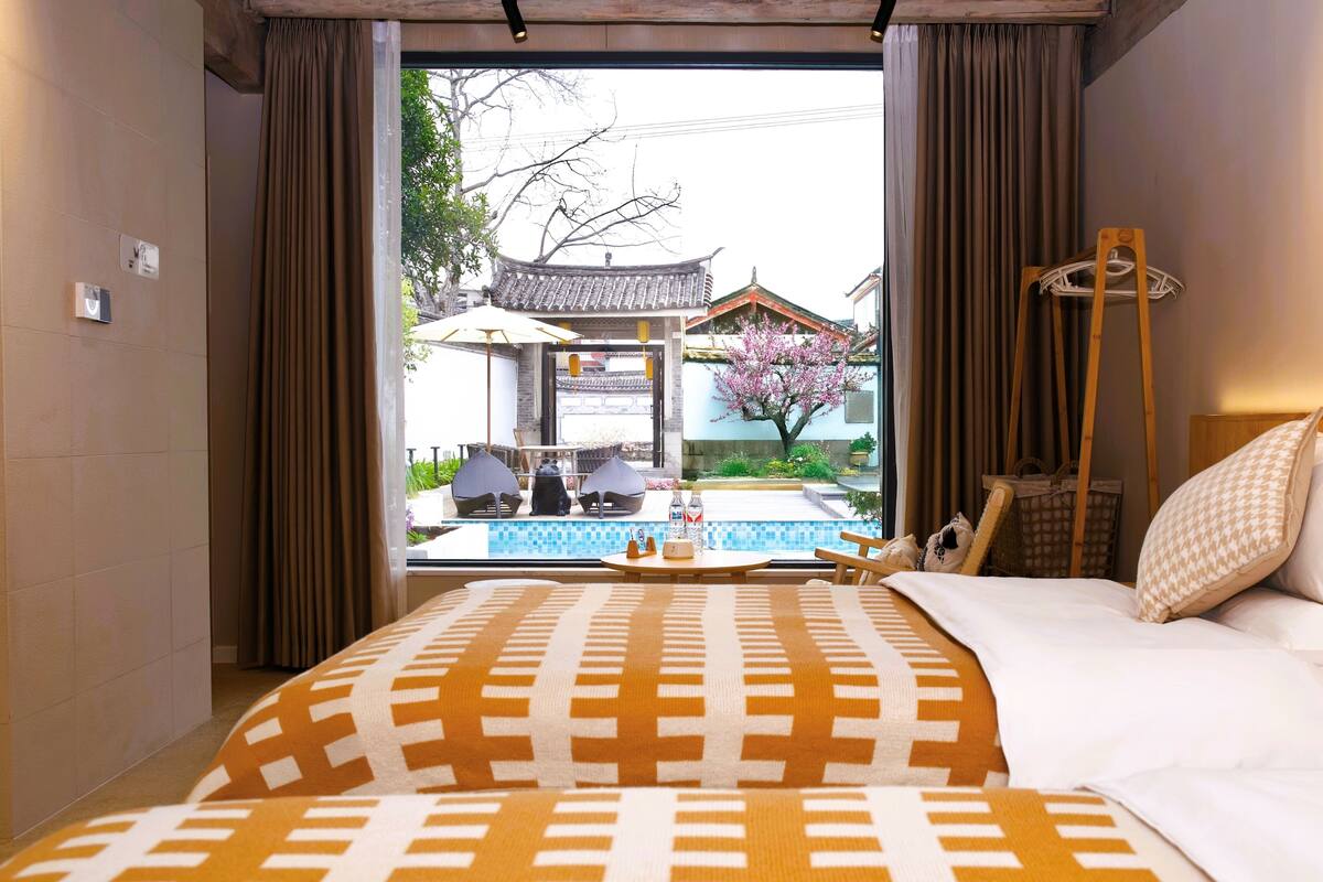 Ein Hotelzimmer mit Bett, Blick auf ein traditionelles Gebäude und einem kleinen Poolbereich.
