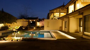 A nighttime view of a traditional Japanese-style house with a swimming pool, outdoor seating, and a well-lit entrance. - Jinghua Inn (Lijiang)