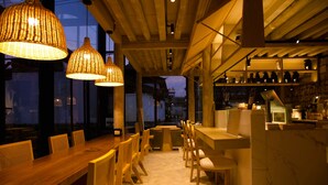 A restaurant with a long wooden table, wicker pendant lights, and a stone wall with shelves. - Jinghua Inn (Lijiang)