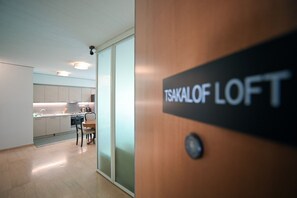 Et moderne interiør med et tekøkken, et spisebord og et skilt med teksten 'TSAKALOF LOFT'.