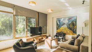 Ein modernes Wohnzimmer mit Flachbildfernseher, Ledersitzmöbeln, einem Couchtisch und einem großen, abstrakten Gemälde an der Wand.