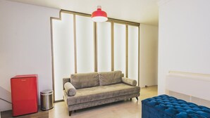 Een moderne woonkamer met een beige bank, een rode koelkast, een blauwe poef en een rode hanglamp.