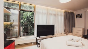 Une chambre d’hôtel moderne dotée d’un grand lit, d’un téléviseur à écran plat, d’un radiateur et offrant une vue sur la verdure grâce à de grandes fenêtres.