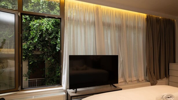 Une chambre d’hôtel avec un lit, un téléviseur posé sur un meuble, un radiateur et une fenêtre avec des rideaux.