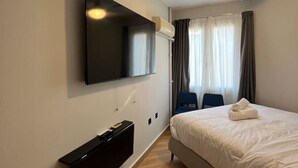 A hotel room with a bed, a flat-screen TV mounted on the wall, a ceiling fan, and a window with curtains. - Aristidou 10 Suite by Zeus suites (Athina)