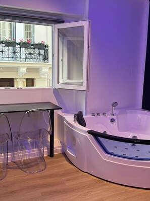 A modern bathroom with a freestanding bathtub, a vanity with a mirror, and a window overlooking a balcony with flowers. - Jacuzzi Platinum Tsakalof 17 (Athina)