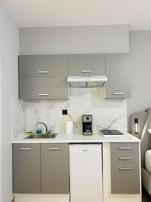 A compact kitchen with grey cabinets, a built-in stove, a coffee maker, and a dishwasher. - Family Suite by Zeussuites (Athina)
