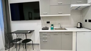 A compact kitchen with grey cabinets, a white countertop, a sink, a kettle, and a black chair.