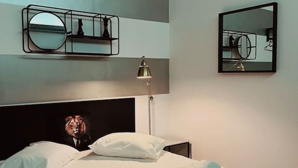 A neatly made bed with a quilted cover, a bedside lamp, and a mirror on the wall.