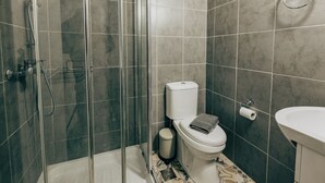 A modern bathroom with a glass-enclosed shower, a toilet, and a sink. - Athenian Suite by Zeus suites (Athina)