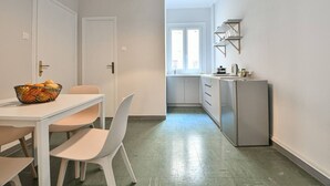 A modern kitchen with white cabinets, a refrigerator, and a dining area with a table and chairs. - Athenian Suite by Zeus suites (Athina)