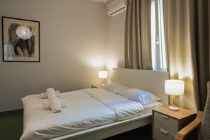 Une chambre d’hôtel comprenant un lit, deux tables de chevet avec des lampes, un climatiseur fixé au mur et une fenêtre avec des rideaux.