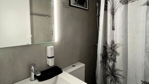 A modern bathroom with a white sink, a toilet, and a shower curtain with a palm leaf pattern. - Muses Suite by Zeus suites (Athina)