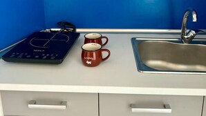 A kitchen with a blue wall, a sink, a stove, and two mugs on the counter.